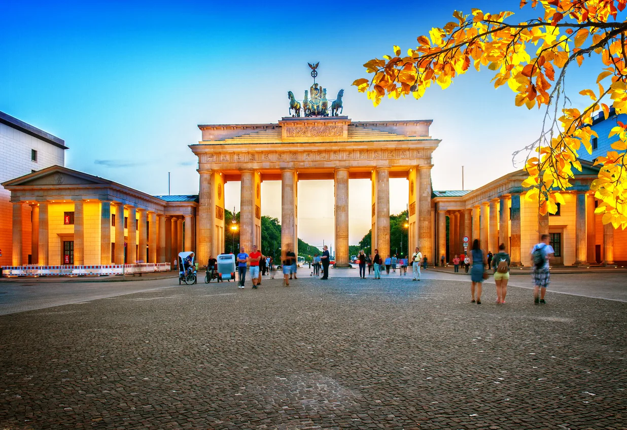 The Brandenburg Gate in Berlin lit up in the evening, framed by autumn leaves