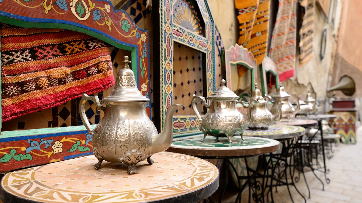 Ornate brass teapots on a carved table in a colourful, lantern-lit Moroccan medina