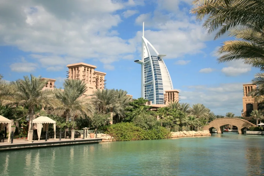 Palm-lined waterways and wind towers at Madinat Jumeirah on the Dubai coast, with the Burj Al Arab beyond