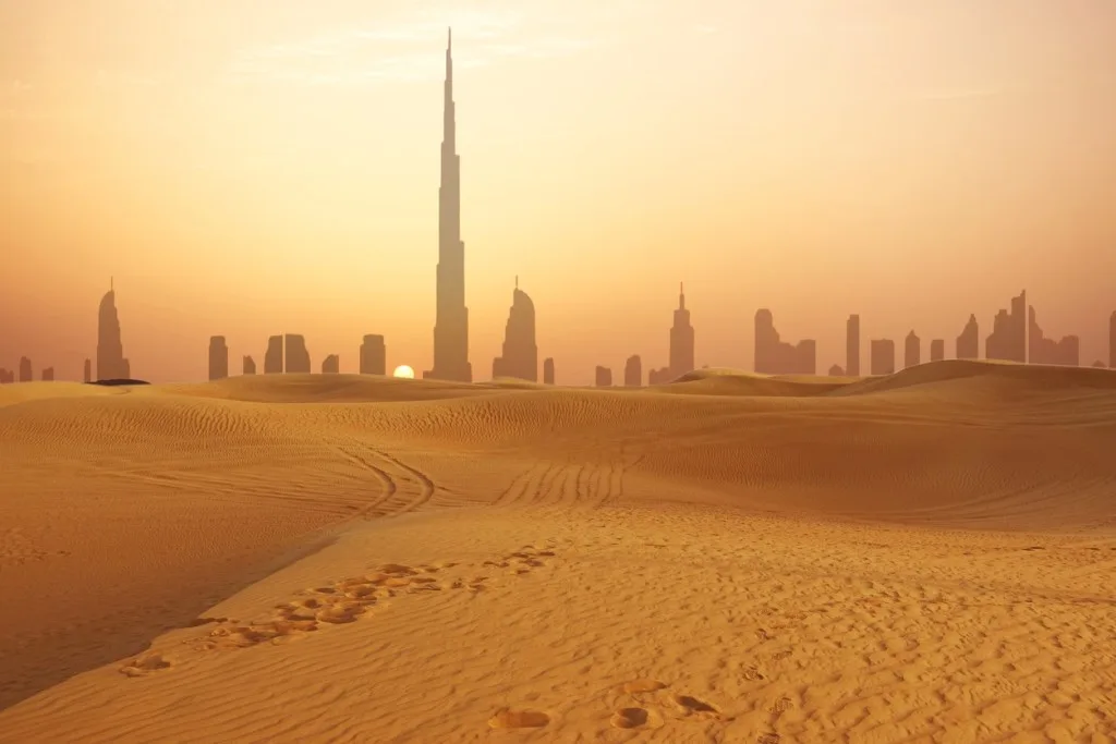The Dubai skyline and Burj Khalifa seen across desert dunes at sunset