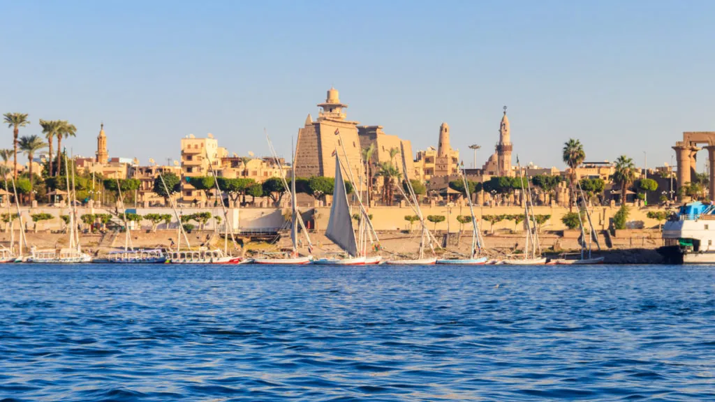 Luxor Temple and the city waterfront seen across the River Nile, with sailing boats moored along the east bank