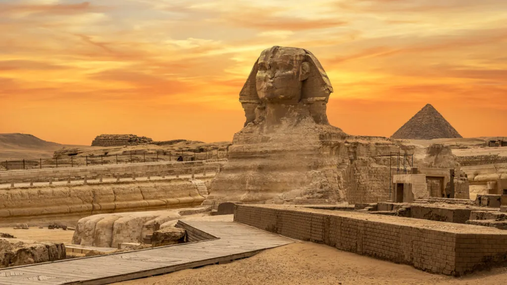 The Great Sphinx and a pyramid at Giza under an orange sunset sky
