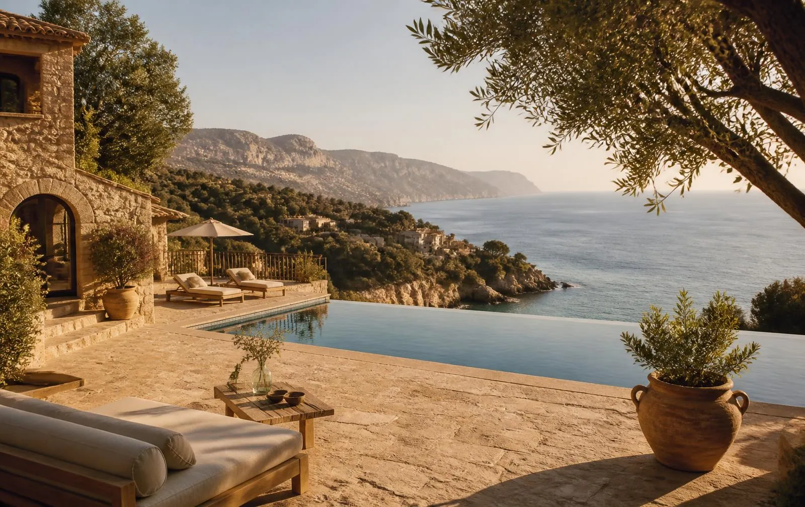 Stone terrace of a Mallorcan coastal retreat property with an infinity pool, olive trees and the Mediterranean beyond