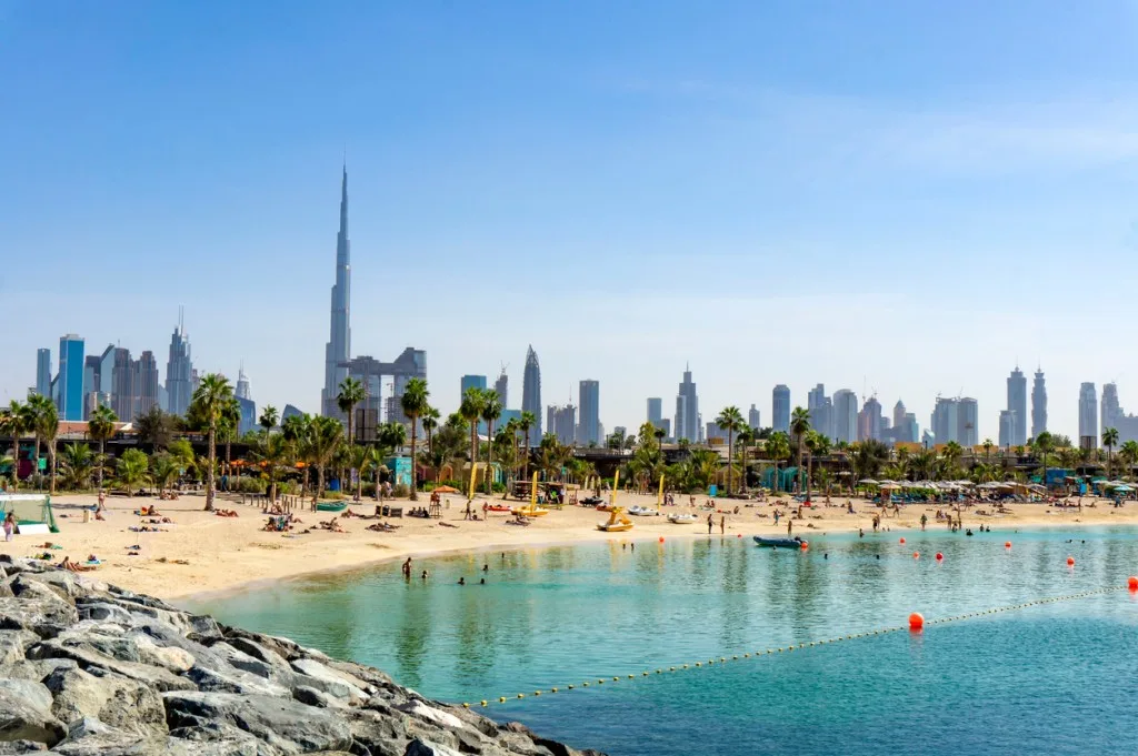 The Dubai skyline and Burj Khalifa rising behind a palm-lined beach and turquoise sea