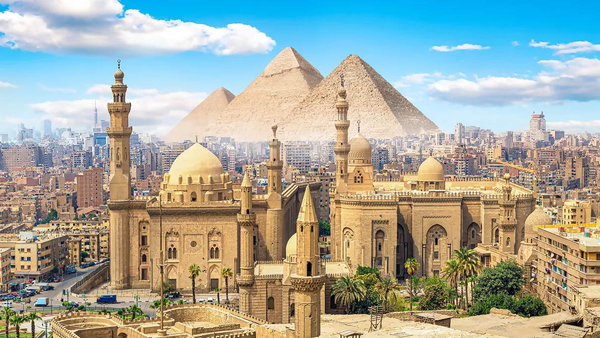 Cairo’s Sultan Hassan Mosque and historic domes, with the Pyramids of Giza rising on the horizon
