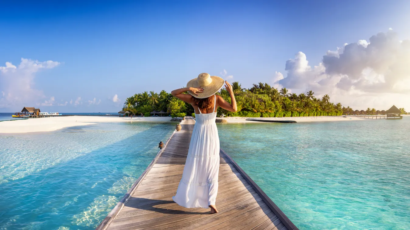 A wooden jetty leading across a shallow lagoon to a palm-covered Maldivian island