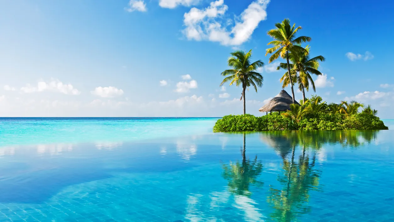 A small palm-fringed island rising from a clear turquoise lagoon in the Maldives