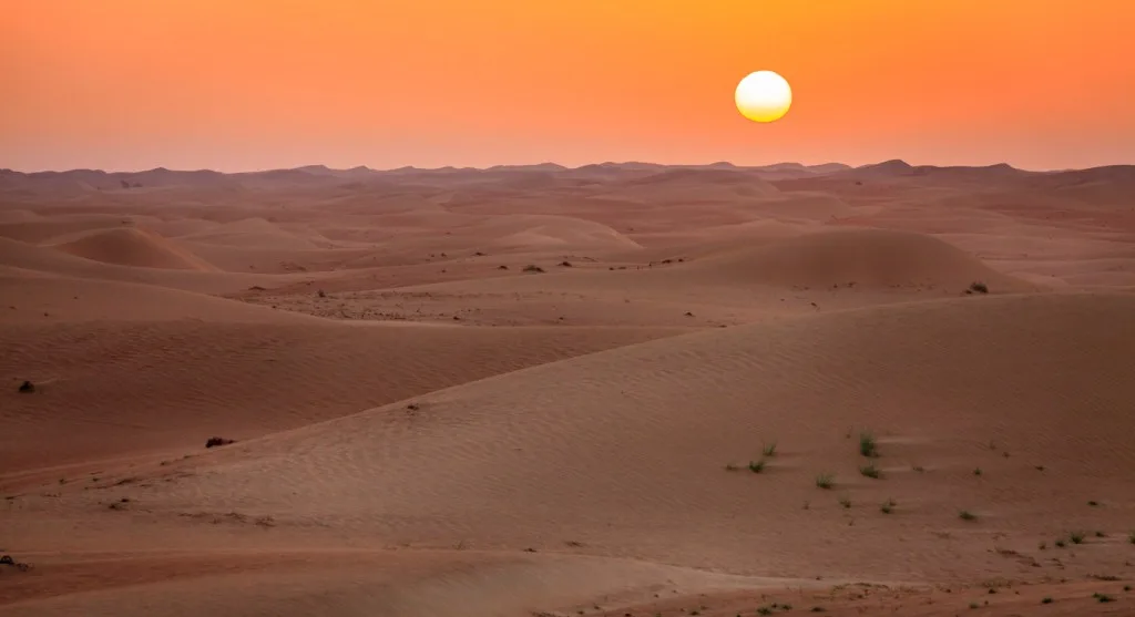 The sun rising over rolling red sand dunes in the desert